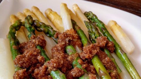 Spargel liegt auf einem weißen Teller, garniert mit einer würzigen Sauce, die das Gericht verfeinert.