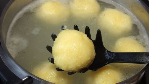 Kartoffelklöße schwimmen im heißen Wasser, während einer von ihnen mit einer Schaumkelle herausgehoben wird.
