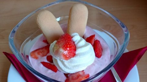 Ein Dessert mit Erdbeeren und Sahne ist in einer transparenten Schüssel angerichtet, dekoriert mit Cookies und frischen Erdbeeren.