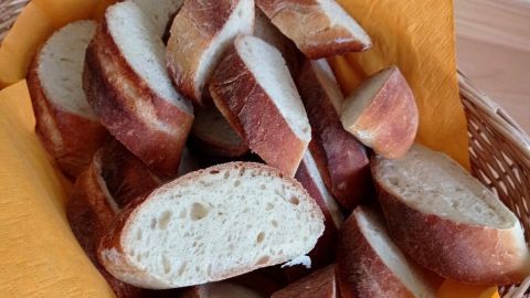 Schnitte von frisch gebackenem Baguette liegen auf einem gelben Serviette in einem geflochtenen Korb auf einem Tisch.