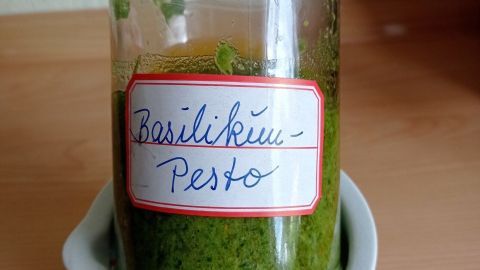 Ein Glas Basilikum-Pesto steht in einer weißen Schale auf einer Holzoberfläche und zeigt eine leuchtend grüne Farbe.