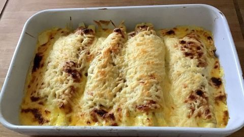 Spargel im Schlafrock wird in einer weißen Auflaufform serviert, überbacken mit geschmolzenem Käse, goldbraun gebräunt.