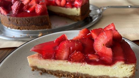 Eine verführerische Erdbeer-Cheesecake-Scheibe liegt auf einem Teller, während eine entspannte Tafel im Hintergrund wartet.