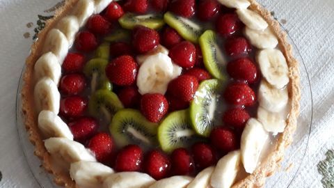 Ein Obstkuchen liegt auf einem Tisch, garniert mit Erdbeeren, Bananen und Kiwis, umgeben von einer gelierenden Schicht.