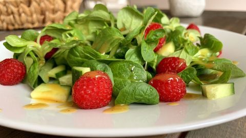 Ein frischer Feldsalat mit Himbeeren und Gurkenstücken wird mit einem Honig-Senf-Dressing angerichtet.