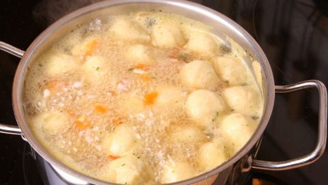 In einem Topf kochen leckere Semmelklößchen in sprudelnder Brühe, umgeben von dampfendem Wasser und Gemüse.