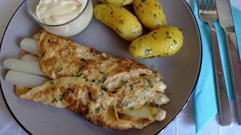 Ein Spargel-Omelette liegt auf einem Teller zusammen mit kleinen, köstlich gewürzten Kartoffeln und einer Portion...