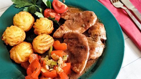 Zarte Putenfilets in Rotwein-Pfeffersoße liegen auf einem grünen Teller, umgeben von Gemüse und knusprigen Beilagen.