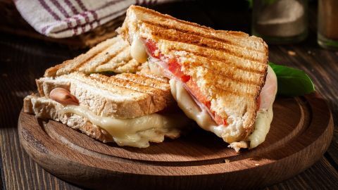 Zwei frisch gegrillte Sandwichtoasts mit Tomate und Schinken liegen auf einem Holzbrett, umgeben von rustikalem Ambiente.