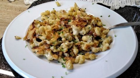 Käsespätzle auf einem weißen Teller mit knusprigem Bacon, serviert auf einem dunklen Tisch, umgeben von Schnittlauch.