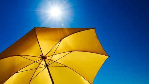 Ein gelber Sonnenschirm steht offen, während die Sonne hell am blauen Himmel scheint, ideal für heiße Temperaturen.