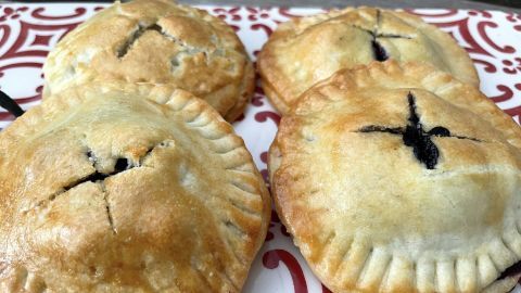 Kleine, goldbraune Blaubeer-Pie-Cookies liegen auf einem dekorativen Teller und zeigen ihre fruchtige Füllung.