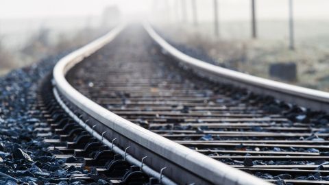Eisenbahnschienen verlaufen geschwungen durch eine neblige Landschaft, die Ruhe und Fernweh vermittelt.