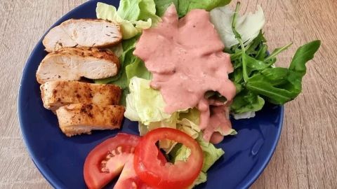 Ein blauer Teller mit frischem Salat, Himbeer-Salatsoße und gegrilltem Hähnchen, dekoriert mit Tomatenscheiben.