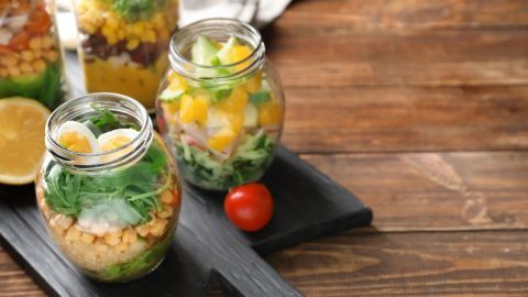 Bunte Salate in Gläsern stehen auf einem Holzbrett, mit frischen Zutaten und einer Zitrone daneben, appetitlich angerichtet.
