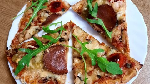Auf einem weißen Teller liegen Pizzastücke mit Champignons und Frühlingszwiebeln, garniert mit Rucola.