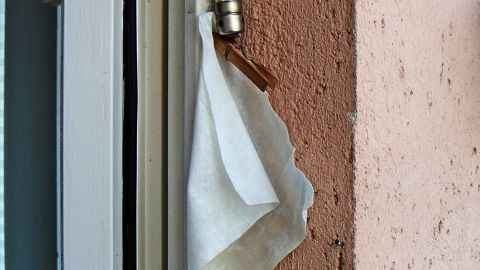 Ein Trocknertuch hängt an einer Wäscheklammer neben einem Thermometer an einer Wand, um Stechmücken abzuwehren.