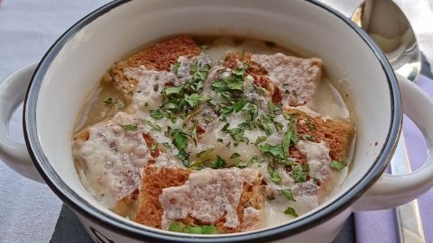 Eine dampfende Schüssel französischer Zwiebelsuppe mit Käse und Croutons, serviert auf einem schwarzen Steinbrett.