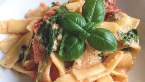 Pasta auf einem Teller: frische Nudeln sind mit einer cremigen Sauce und Basilikum garniert, appetitlich angerichtet.