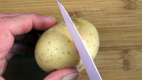 Pellkartoffeln leichter schälen - probiert mal folgenden Trick: Rohe Kartoffeln außenherum mit einem scharfen Messer die Schale dünn einschneiden. Eine Hand hält eine Kartoffel, während ein Messer an der Schale einritzt, um das Schälen zu erleichtern.