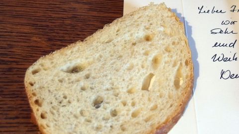 Eine Scheibe Weißbrot liegt auf einem handgeschriebenen Brief auf Holz. Text: "Lieber Besucher, wir sind umgezogen."