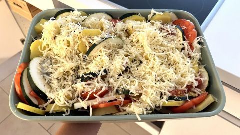 Ein Auflauf aus Kartoffeln, Zucchini und Tomaten wird in einer grünen Form mit Käse überbacken.
