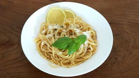 Eine Schüssel Zitronennudeln, die mit frisch geriebenem Parmesan und Basilikum garniert und mit Zitronenscheiben dekoriert ist.