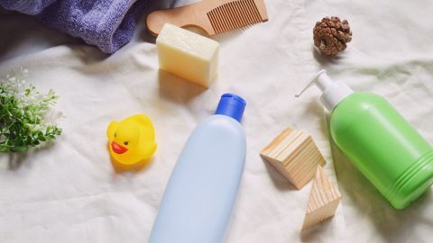 Eine blaue Flasche Duschgel und eine grüne Flasche Shampoo liegen auf einem weißen Tuch, umgeben von Accessoires.