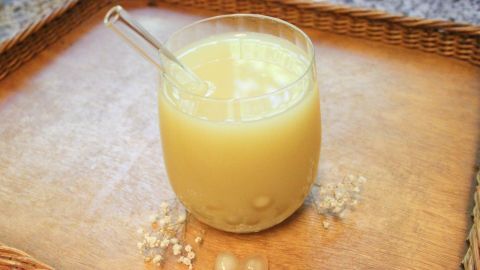 Ein Glas Bubble Tea steht auf einem Holztablett, mit einer Strohhalm und Tapiokaperlen daneben, in einer hellen Umgebung.