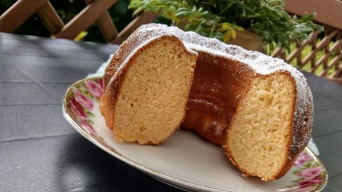 Ein frisch geschnittenes Stück Mascarponekuchen liegt auf einem weißen Teller, umgeben von einem blühenden Pflanze im Hintergrund.