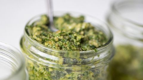 Ein Glas mit grünem Kräuter-Hanfsamen-Pesto wird appetitlich präsentiert, umgeben von weiteren Gläsern in einem hellen Umfeld.