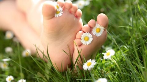 Barfußfüße liegen im Gras, geschmückt mit Gänseblümchen, was eine entspannte Atmosphäre der Selbstpflege schafft.