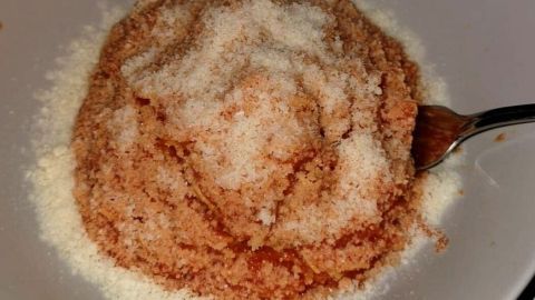 Ein Teller enthält eine dickflüssige Minestrone, die mit einer Schicht von feinem Käse überzogen ist. Ein Löffel liegt daneben.