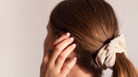 Ein Hand greift nach dem schimmernden Haar, das zu einem hohen Pferdeschwanz gebunden ist, während ein Haargummi sichtbar ist.