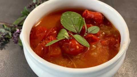 Eine Schüssel mit Cherrytomaten-Sugo, die roten Tomaten schwimmen in einer würzigen Soße, garniert mit frischen Kräutern.