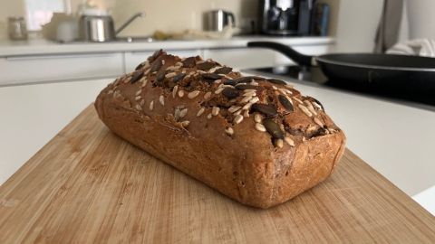 Ein knuspriges Roggenvollkorn-Sauerteigbrot liegt auf einem Holzbrett in einer modernen Küche mit hellen Möbeln.