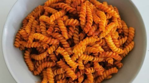 Eine Schüssel mit leuchtend orangefarbener Nudeln steht auf einem Tisch, dekoriert mit einer würzigen Soße.