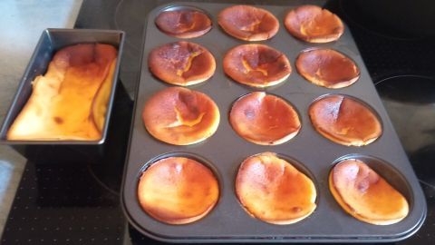 Käsekuchen-Muffins und ein kleiner Kuchen sind leicht gebräunt in der Backform, auf einer Küchenoberfläche platziert.