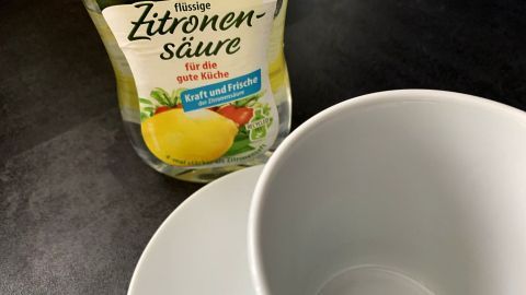 Eine weiße Tasse steht bereit, während Zitronensäure als Reinigungsmittel zur Beseitigung der Teeränder verwendet werden kann.