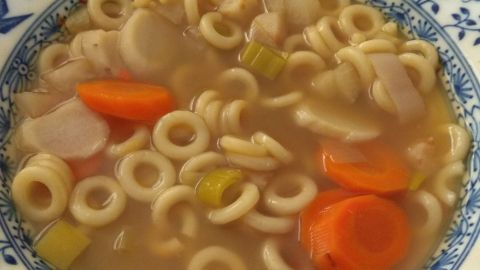 Eine Schüssel mit buntem Nudelgemüse in Brühe steht auf einem Tisch, bereit zum Essen und richtig aufbewahren.