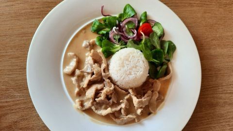 Geschnetzeltes liegt neben einem perfekten Reisboot und einem frischen Feldsalat auf einem weißen Teller.