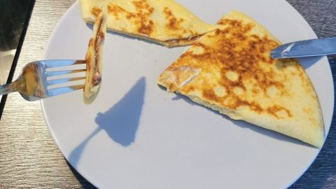 Ein Crêpe mit Kinderschokolade liegt auf einem Teller, während eine Gabel ein Stück davon aufnimmt.