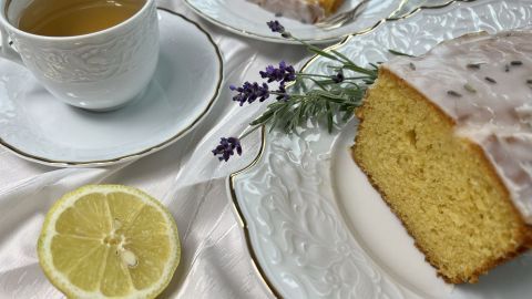 Ein saftiger Zitronen-Lavendel-Kuchen mit Joghurt liegt auf einem eleganten Teller, umgeben von Tee und frischer Zitrone.