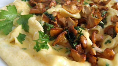 Eine Pfanne zeigt gebratene Pfifferlinge und Eier, garniert mit frischer Petersilie, appetitlich angerichtet auf einem Teller.