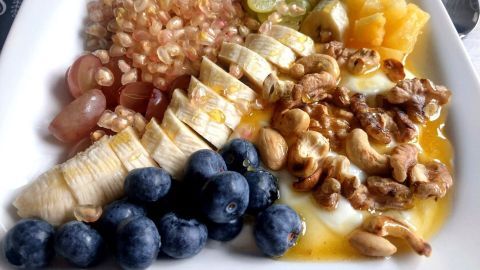 Eine bunte Frühstücks-bowl enthält frisches Obst, Nüsse und Quinoa in einer weißen Schale, perfekt für eine gesunde Mahlzeit.