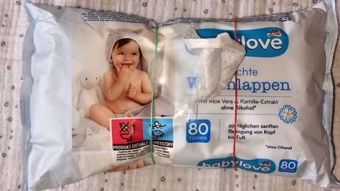 Ein Paket mit Feuchttüchern liegt auf einem Bett. Es zeigt ein lächelndes Baby mit einem Hasen, während die Tücher bereit sind.