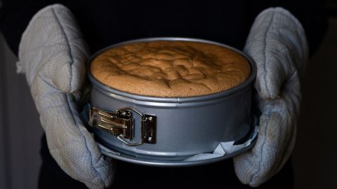 Eine Person hält eine runde Backform mit einem frisch gebackenen Kuchen in der Küche, bereit zum Servieren.