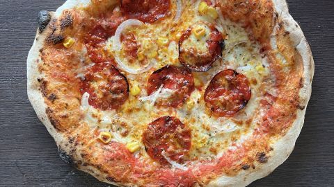Eine frisch gebackene Pizza liegt auf einem dunklen Holztisch und duftet köstlich nach Tomatensauce und Käse.