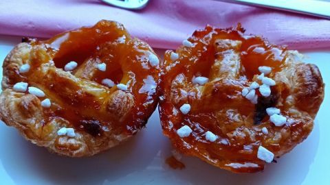 Zwei goldbraune Aprikosen-Blätterteiggebäckstücke liegen auf einem weißen Teller, dekoriert mit Zuckerperlen.
