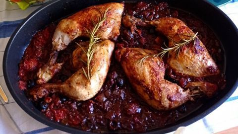 Saftige mediterrane Hähnchenkeulen liegen in einer Pfanne, umgeben von Brot, Wein und Geschirr auf einem Tisch.